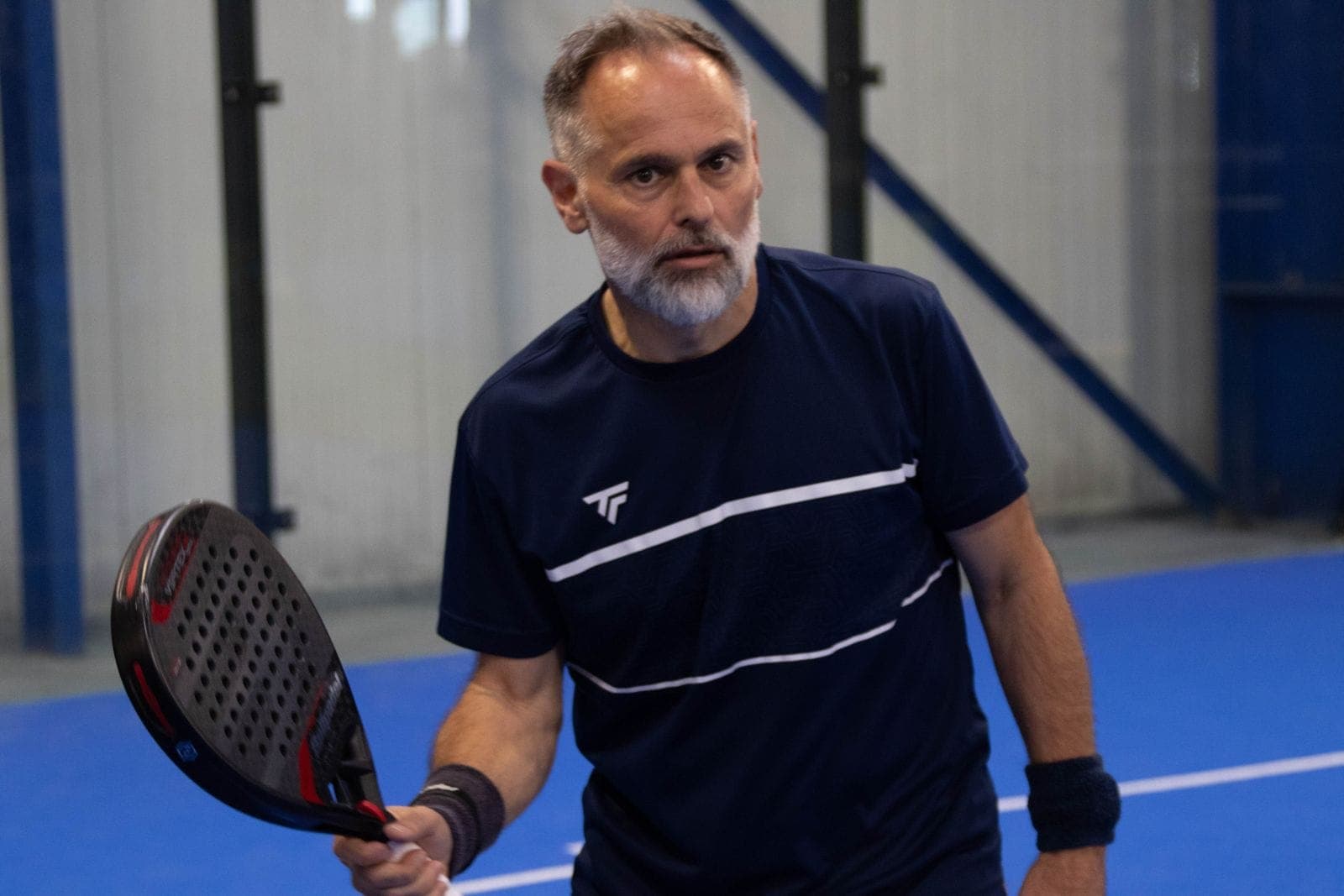 Joueur de padel concentré, raquette en main, sur un terrain bleu de l’Arena