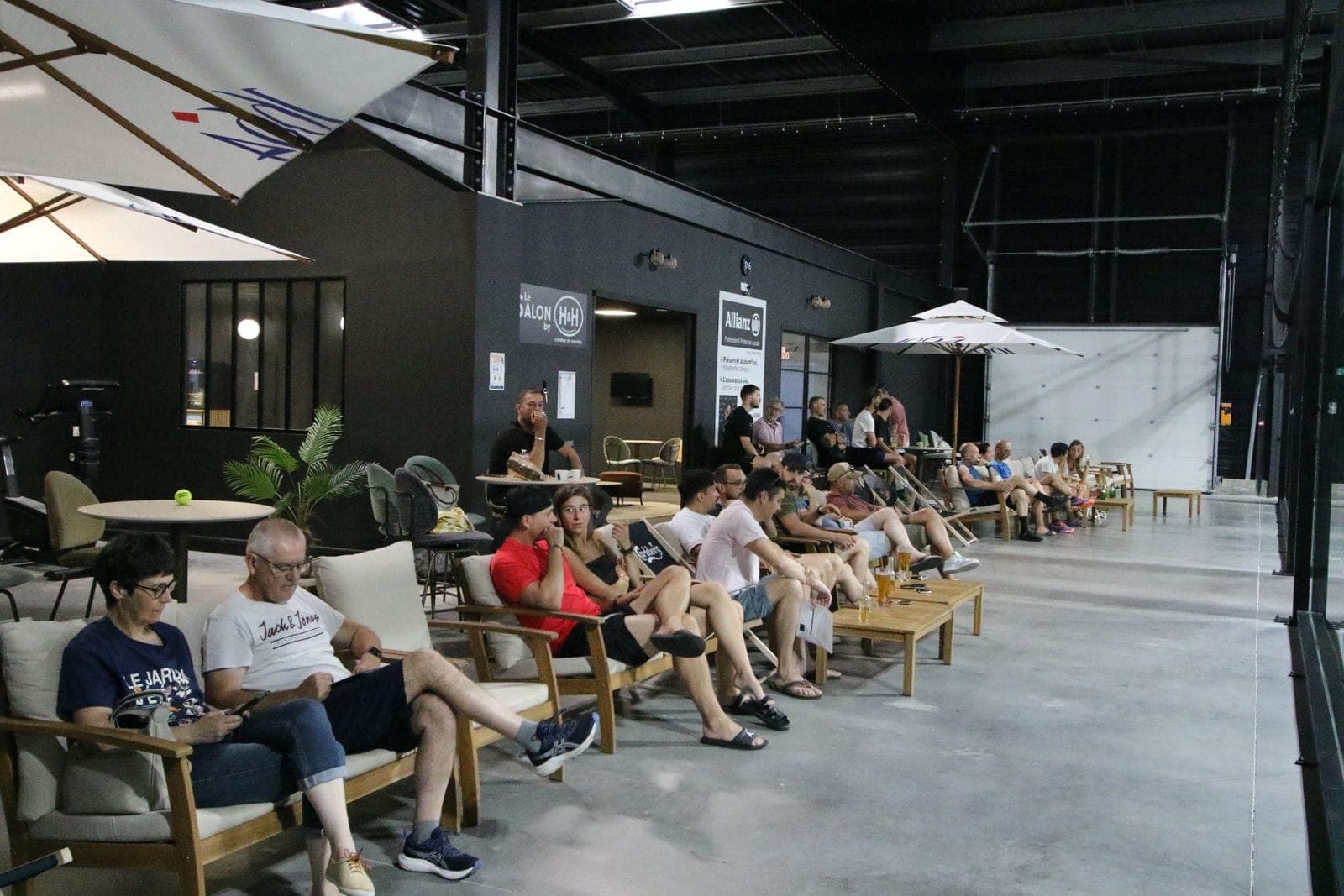 Spectateurs détendus dans des fauteuils lounge, au bord des terrains noirs de l’Arena Complexe