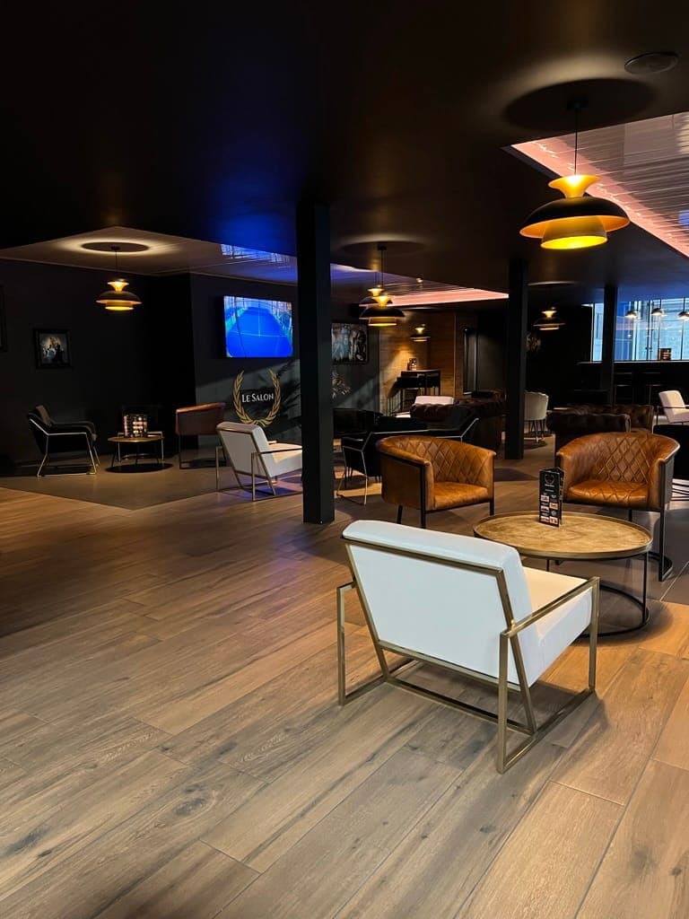 Le Salon, club-house de l’Arena : fauteuils en cuir, suspensions dorées et parquet