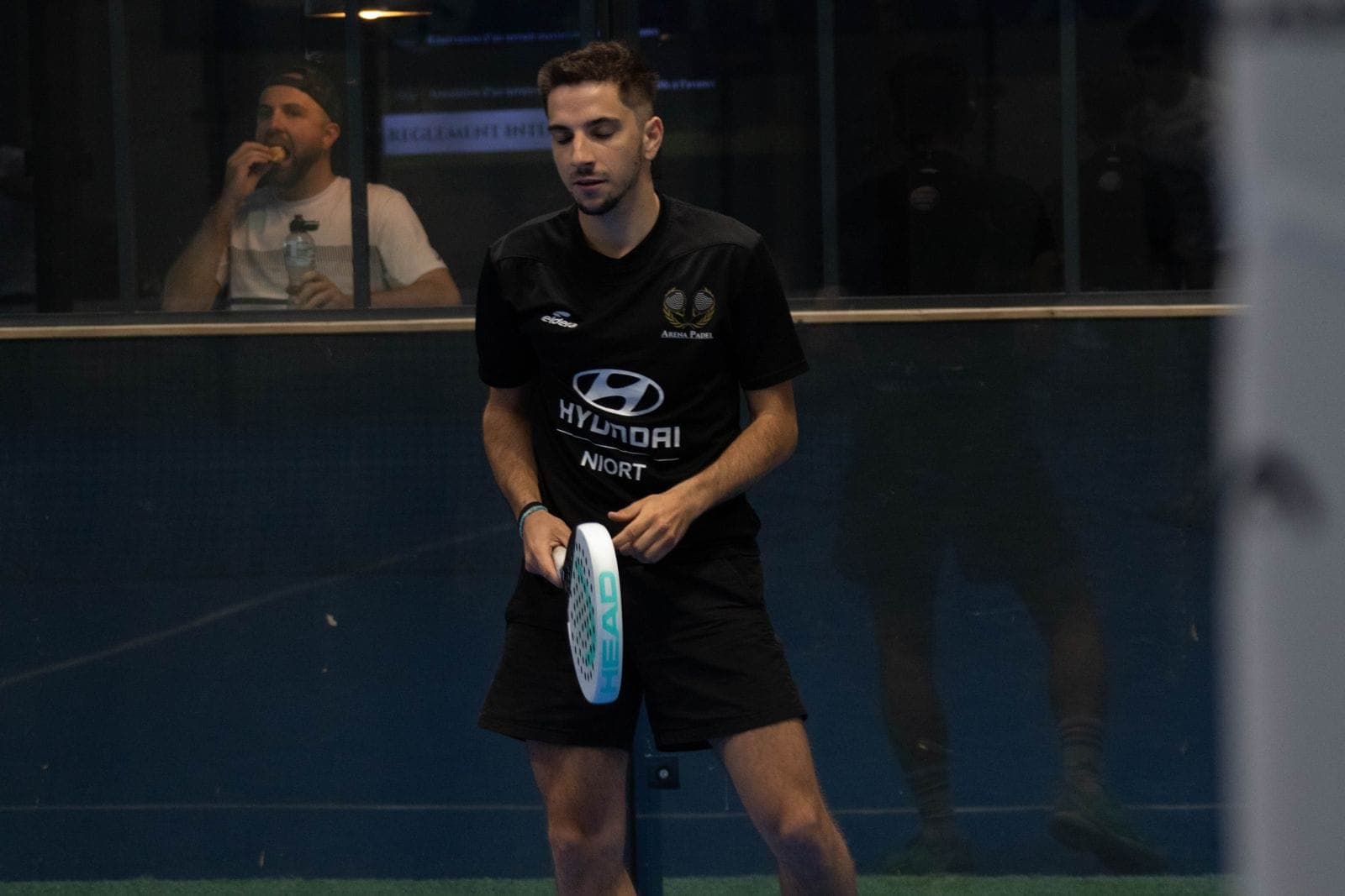 Joueur de l’Arena portant le maillot noir du club, une raquette HEAD à la main