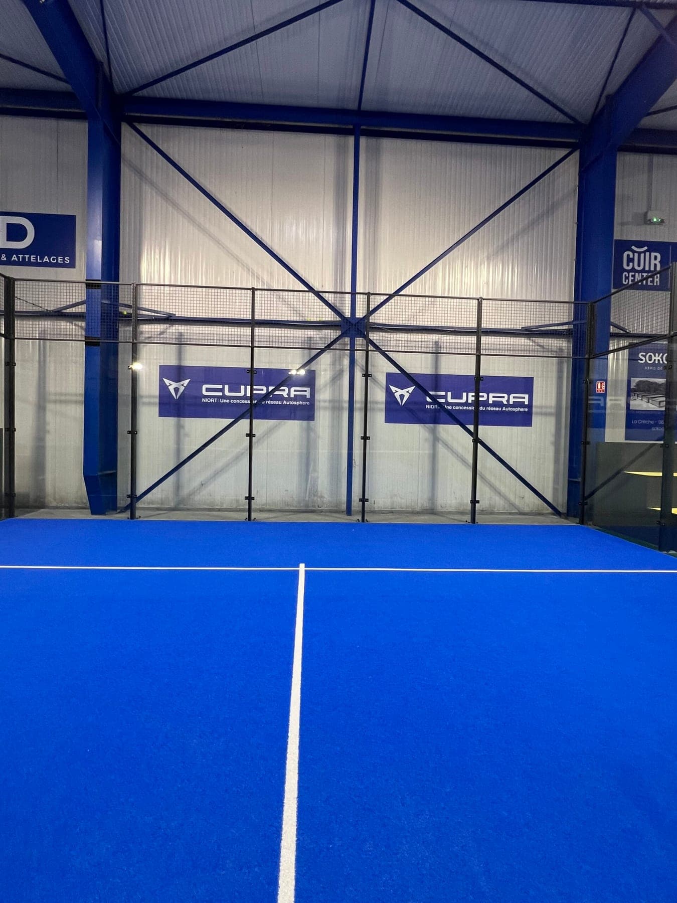 Terrain de padel bleu de l’Arena Padel, sous la charpente métallique